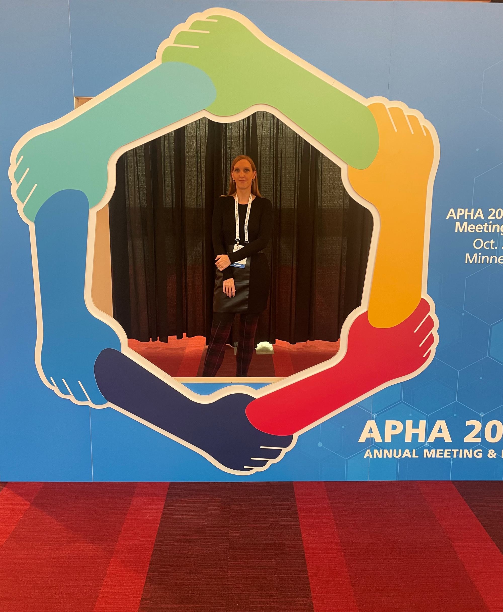 A woman stands in a colorful hands-themed photo booth at the APHA 2023 Annual Meeting in Minnesota, promoting collaboration and community.